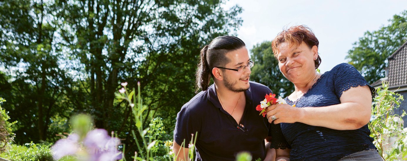junger Mann überreicht älterer Frau Blumen. Text: Demenz braucht Zuneigung junger Mann überreicht älterer Frau Blumen. Text: Demenz braucht Zuneigung