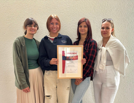 Vier junge Damen blicken in die Kamera, die beiden in der Mitte halten die Gewinnerurkunde in den Händen