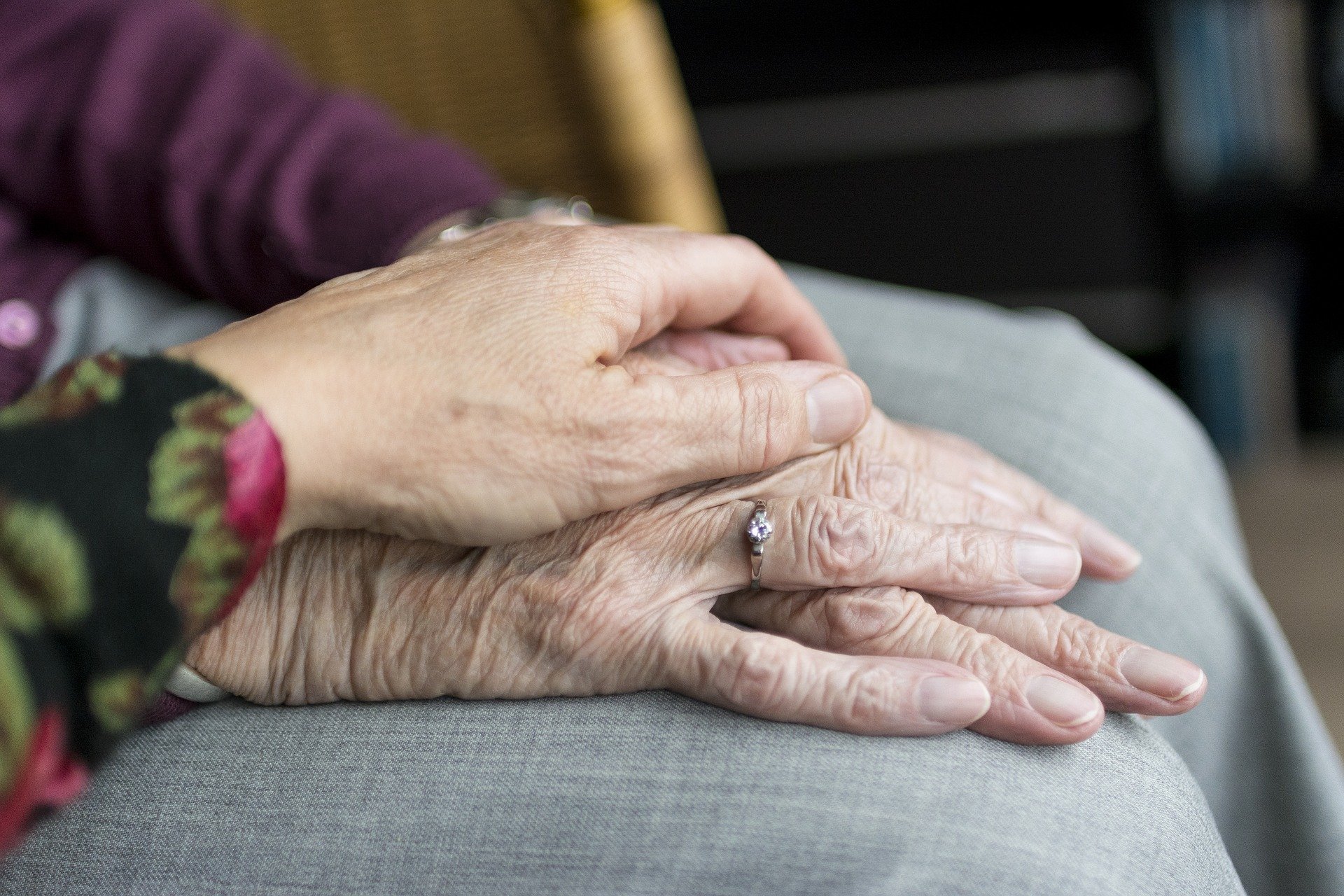 Eine Frau legt ihre Hand auf die Hände einer etwas älteren Dame, und hält sie liebevoll.